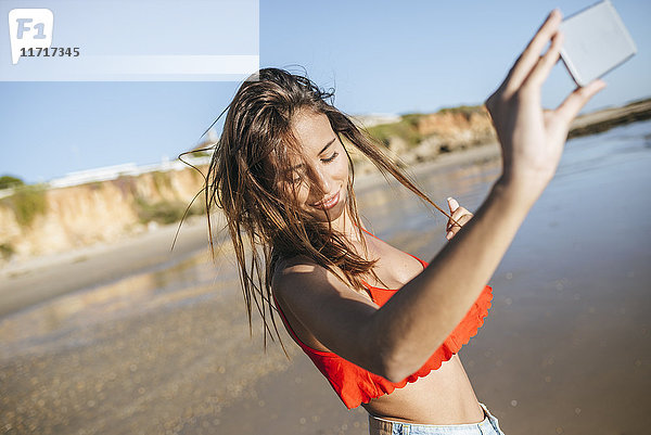 Junge Frau nimmt Selfie am Strand mit Smartphone mit