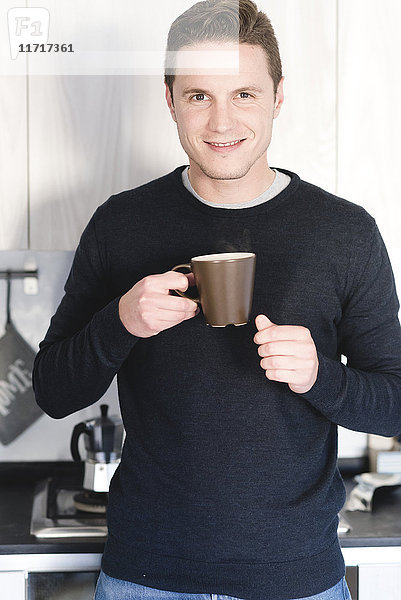 Porträt eines lächelnden Mannes mit einer Tasse Kaffee in der Küche