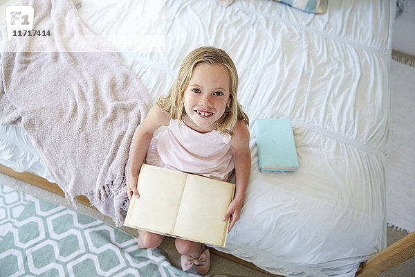 Porträt eines kleinen Mädchens auf dem Bett sitzend mit Buch