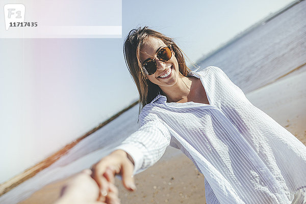Porträt einer lächelnden jungen Frau mit Sonnenbrille am Strand