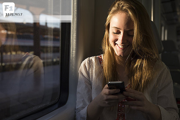 Lächelnde junge Frau im Zug beim Blick aufs Handy