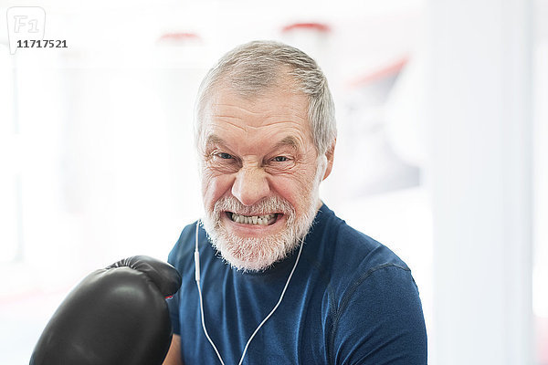 Porträt eines aggressiven Senioren mit Kopfhörern und Boxhandschuhen im Fitnessstudio