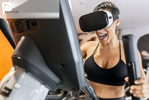 Frau mit VR-Brille auf einem Ellipsentrainer in der Turnhalle