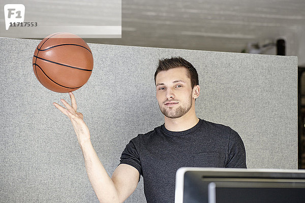 Junger Mann  der im Büro arbeitet und einen Basketball balanciert.