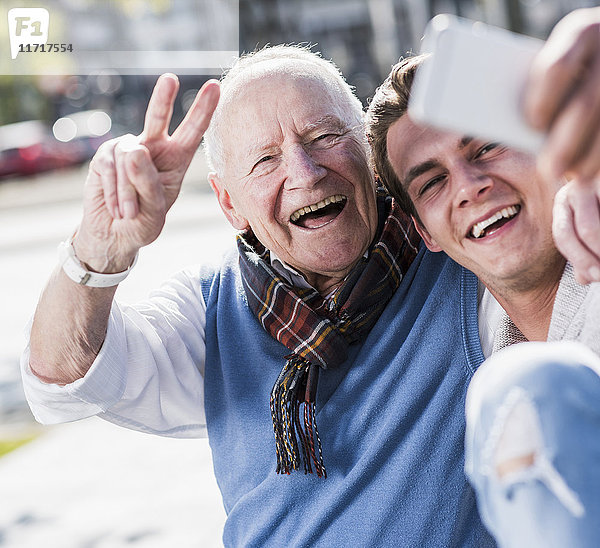 Glücklicher älterer Mann und erwachsener Enkel  der einen Selfie nimmt.