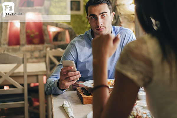 Mann mit Handy von Angesicht zu Angesicht mit seiner Freundin in einem Restaurant