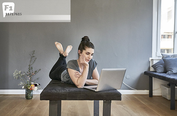 Junge Frau im Wohnzimmer liegend mit Laptop
