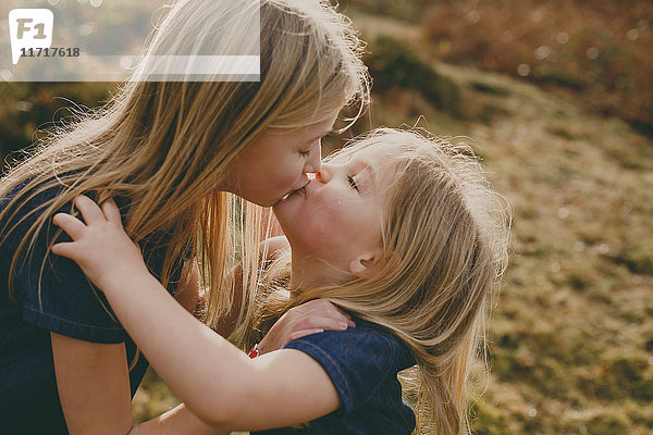 Zwei süße blonde Schwestern  die sich draußen küssen.