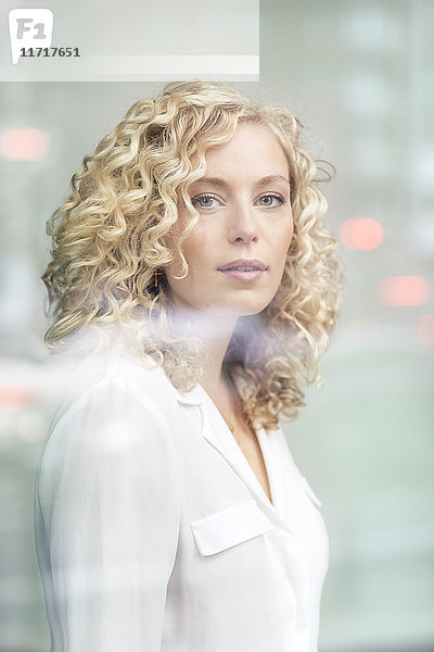 Porträt einer blonden Geschäftsfrau hinter der Fensterscheibe