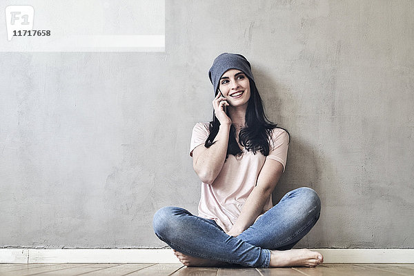 Lächelnde junge Frau sitzt auf dem Boden und redet am Handy.