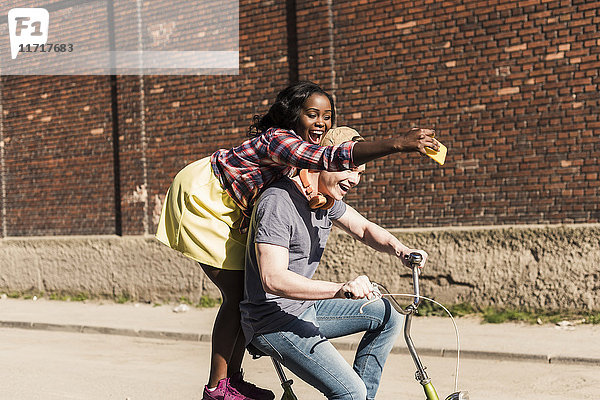 Junges Paar  das auf der Straße Fahrrad fährt  Frau  die auf einem Gestell steht und sich selbst mitnimmt.