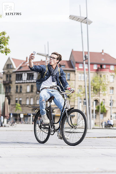 Verspielter junger Mann mit Fahrrad in der Stadt per Handy