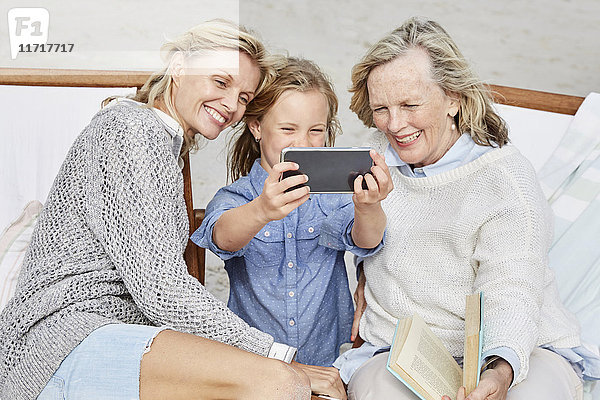 Mutter  Tochter und Großmutter mit Smartphone am Strand