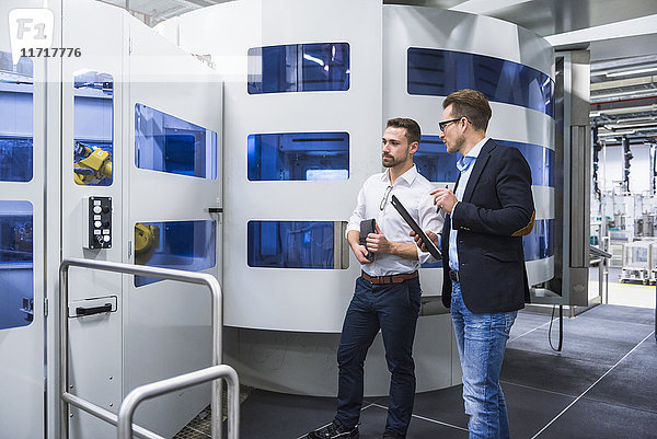 Zwei Männer  die in der Fabrikhalle reden und die Maschine ansehen.