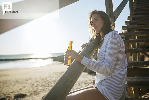 Junge Frau mit einer Flasche Bier zum Entspannen am Strand bei Sonnenuntergang