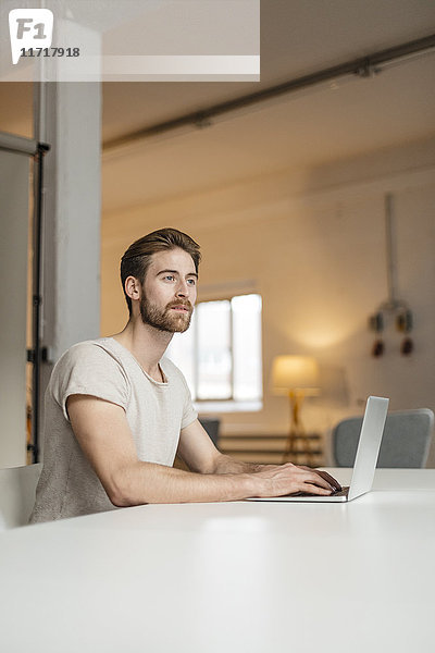 Porträt eines jungen Mannes  der auf einem Laptop in einem Loft arbeitet.