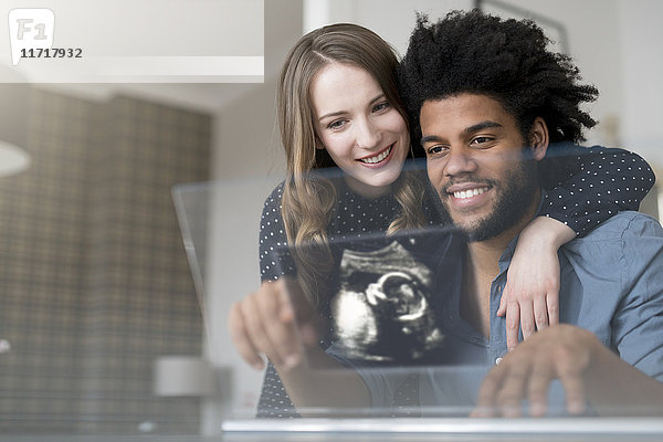 Lächelndes Paar schaut sich das Ultraschallbild des Babys auf einem futuristischen Bildschirm an.