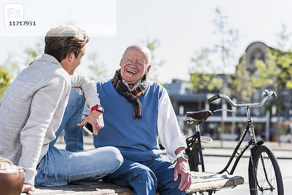 Lachender älterer Mann mit erwachsenem Enkel auf einer Bank