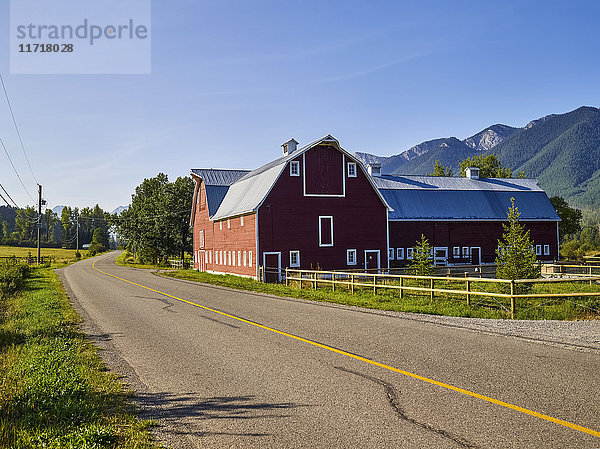 Eine große rote Scheune neben einer Landstraße und eine Bergkette im Hintergrund; Alberta  Kanada'.