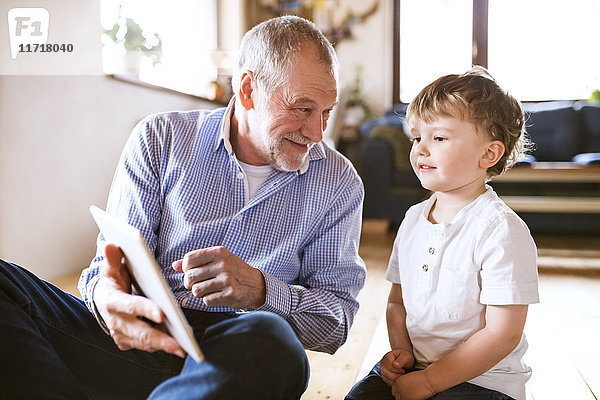 Großvater und Enkel auf dem Boden sitzend  mit digitalem Tablett