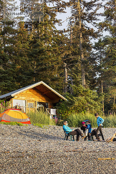 Zwei Frauen und Kinder am Strand mit einer öffentlich zugänglichen Hütte des National Forest Service im Hintergrund  Hekseth Island  Southcentral Alaska  USA