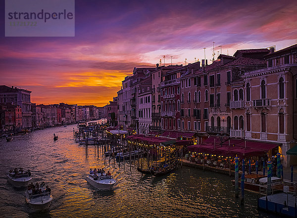 Ein dramatischer und farbenfroher Sonnenuntergang über dem Kanal und den Gebäuden  mit Wassertaxis im Kanal; Venedig  Italien'.
