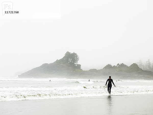 Ein Surfer im Neoprenanzug geht am Wasser entlang  Cox Bay; Tofino  British Columbia  Kanada'.