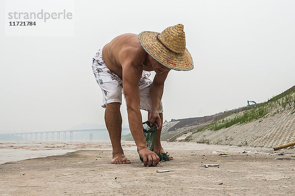 Ein Fischer bei der Arbeit mit seinem Netz  um einige kleine Fische im Jangtse-Fluss zu fangen; Chongqing  China'.