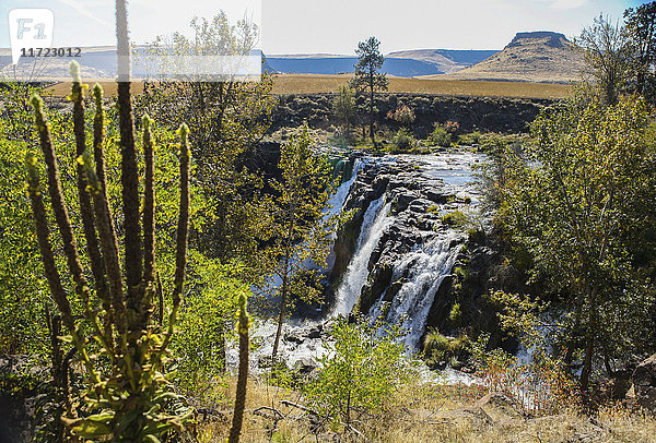 Wasserfall über einer Klippe mit einem Feld und Hochebenen in der Ferne