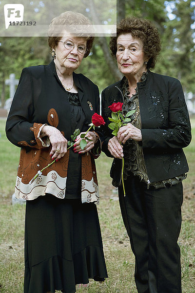 Zwei Frauen halten einzelne rote Rosen auf einem Friedhof; Edmonton  Alberta  Kanada'.
