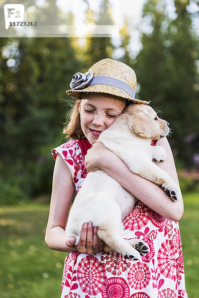 Ein junges Mädchen in Sonnenkleid und Hut hält einen Labrador-Welpen im Arm; Anchorage  Alaska  Vereinigte Staaten von Amerika'.