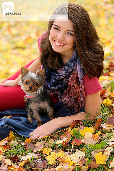 Eine junge Frau sitzt mit ihrem Hund im Herbst auf dem mit Blättern bedeckten Gras; Oregon  Vereinigte Staaten von Amerika'.