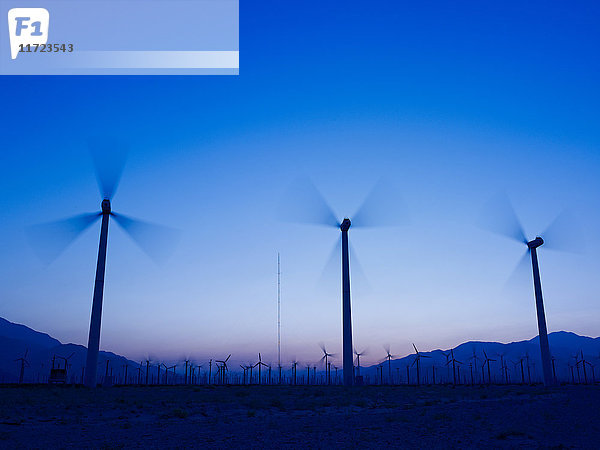 Silhouette von Windkraftanlagen in einem Feld mit einer Bergkette in der Ferne bei Sonnenuntergang; Palm Springs  Kalifornien  Vereinigte Staaten von Amerika'.