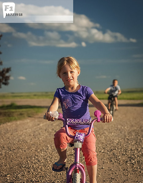 Ein junges Mädchen fährt mit ihrem Fahrrad eine Schotterstraße hinunter  ihr Bruder fährt hinterher; Herschel  Saskatchewan  Kanada'.