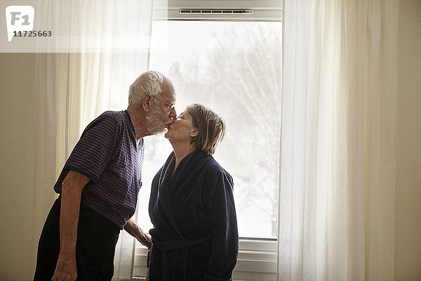 Älteres Paar küsst sich neben dem Fenster