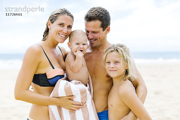 Familie mit zwei Kindern (12-17 Monate  8-9)  die sich am Strand umarmen