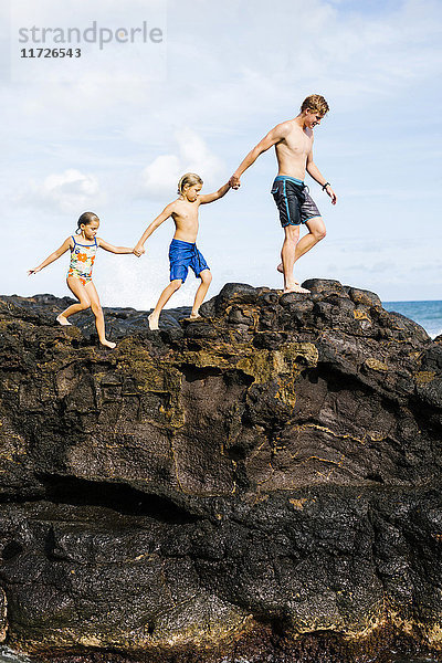 Junger Mann geht mit Kindern auf einem Felsen (6-7  8-9)