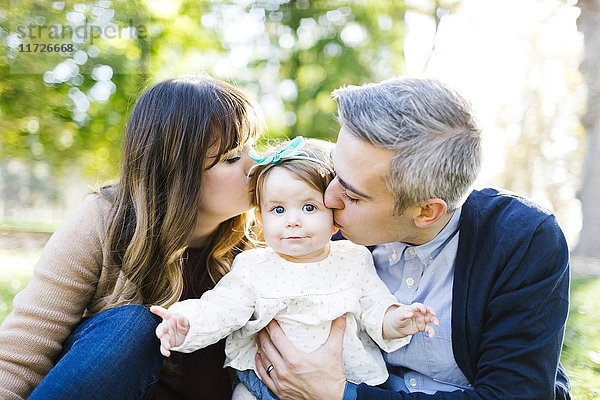Porträt der Eltern  die ihre Tochter (12-17 Monate) im Park küssen