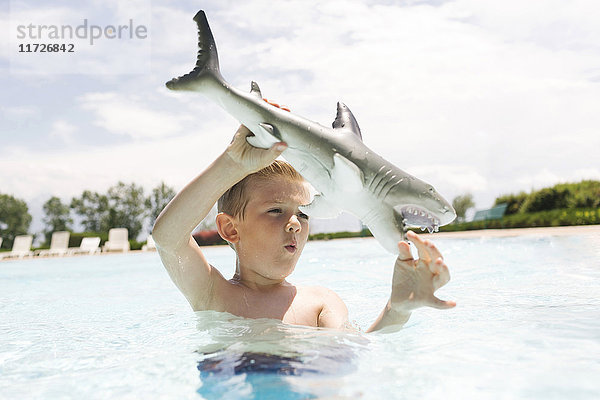 Junge (6-7) spielt mit Spielzeug-Hai im Schwimmbad