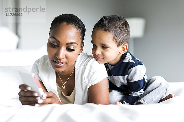 Mutter und Sohn (2-3) liegen auf dem Bett und benutzen ein Smartphone