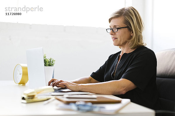 Reife Frau im Büro tippt auf Laptop