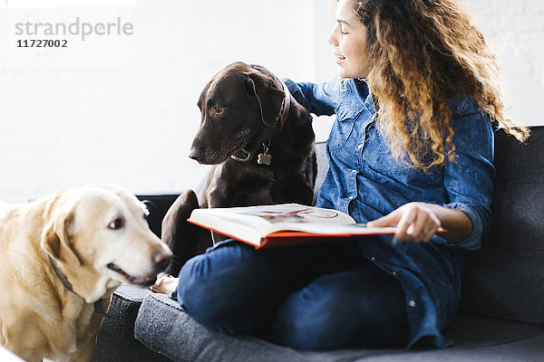 Frau sitzt mit Hunden im Wohnzimmer und liest ein Buch