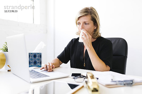 Frau benutzt Laptop  schnäuzt sich die Nase