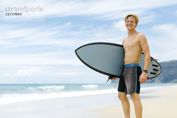 Mann steht am Strand und hält Surfbrett