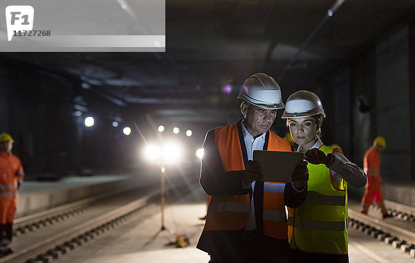 Vorarbeiter und Bauarbeiter mit digitalem Tablett auf dunkler unterirdischer Baustelle