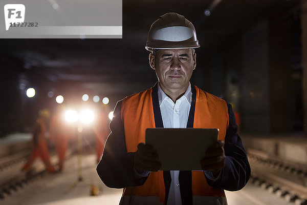 Seriöser Vorarbeiter mit digitalem Tablett auf dunkler Baustelle