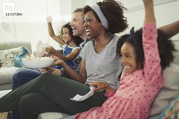 Enthusiastische  multiethnische junge Familie beim Jubeln  Sport auf dem Sofa schauen
