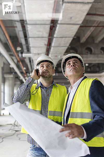 Männliche Ingenieure mit Taschenlampe und Bauplänen beim Blick auf die Baustelle