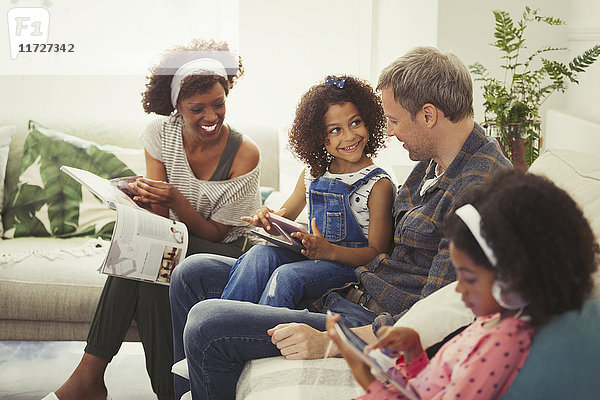 Multiethnische junge Familie mit digitalen Tabletts und Lesemagazin auf dem Sofa