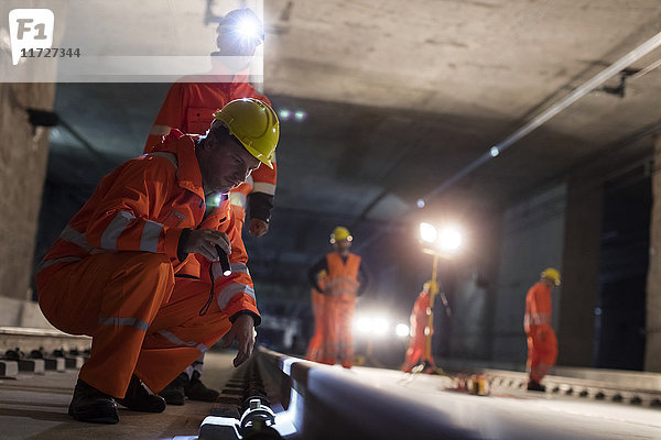 Männliche Bauarbeiter untersuchen unterirdische Gleise auf dunkler Untergrundbaustelle